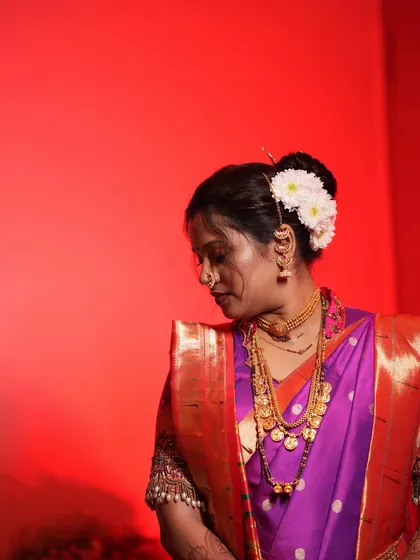 A side profile showcasing the elegant bridal bun adorned with fresh white flowers and a traditional hair accessory. The makeup is subtle, with a focus on flawless skin.
