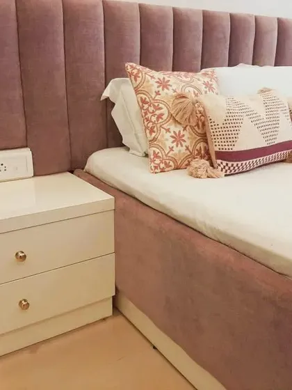 The finish of your furniture makes all the difference. This image highlights a custom-made bed with a plush, channel-tufted velvet headboard and a glossy white side table, showcasing our commitment to high-quality craftsmanship.