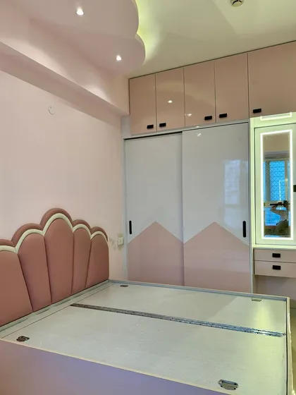 For this kids' bedroom, we created a playful yet elegant space. The design includes a custom scalloped headboard in pink velvet, a matching two-tone sliding wardrobe, and an integrated dressing unit with a backlit mirror.