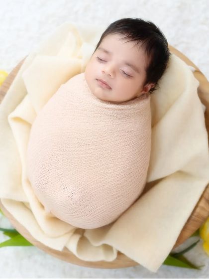 A sleeping newborn swaddled in a neutral wrap and placed in a wooden bowl with yellow tulips. A simple, organic, and beautiful composition.