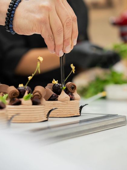 Using tweezers, a chef delicately places garnishes on a complex pastry, a testament to the fine motor skills developed in our classes.
