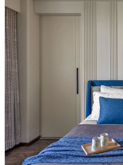 A calm and comfortable bedroom design. The deep blue upholstered bed is set against a wall with simple vertical paneling, creating a serene and structured look.