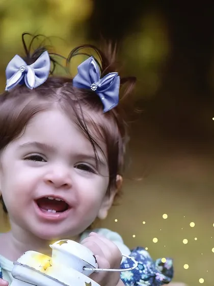 A close up shot of a happy one year old girl with cute pigtails and a bright smile, holding a glowing lantern.