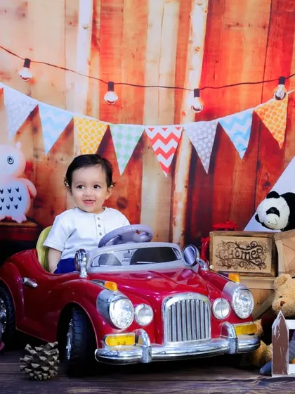 A classic first birthday shot with a baby in a toy car, a "ONE" sign, and a festive background. A perfect way to mark the milestone.
