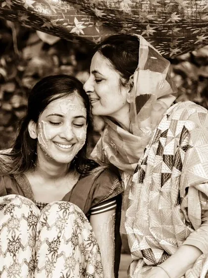 A mother's love captured during the Haldi ceremony. This sepia-toned photo shows a mother whispering to her smiling daughter, a precious and intimate family moment.