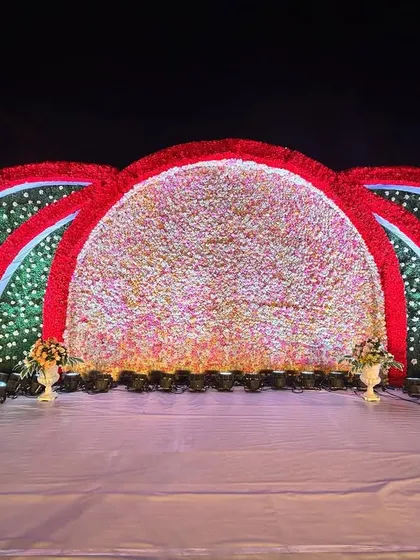 This reception stage is a celebration of color, with massive arches covered in red and multi-colored flowers. The design creates a dramatic and festive backdrop for a grand celebration.