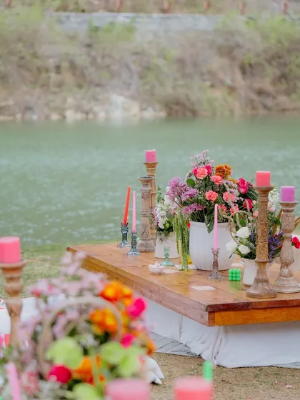 A lakeside table setting from the 'Sunny Sway Soirée'. The vibrant floral centerpieces and colorful candles popped against the serene water backdrop.