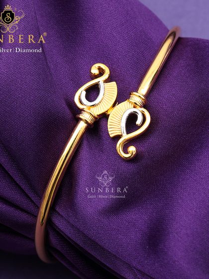 An elegant gold open-cuff bracelet with paisley-shaped terminals in a two-tone finish. This design blends traditional motifs with modern style, making it a versatile accessory.