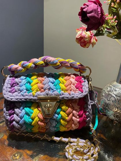 The rainbow crochet bag styled on a wooden table, showing how it can be a beautiful decorative object even when you're not carrying it.