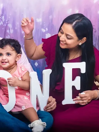A happy family of three posing with 'ONE' letters to celebrate their daughter's first birthday milestone.