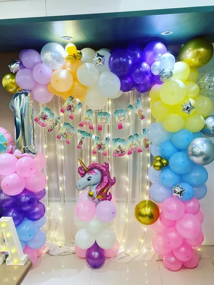 A close-up of the Unicorn birthday backdrop, with a "Happy Birthday" banner, fairy lights, and a mix of pastel and metallic balloons.