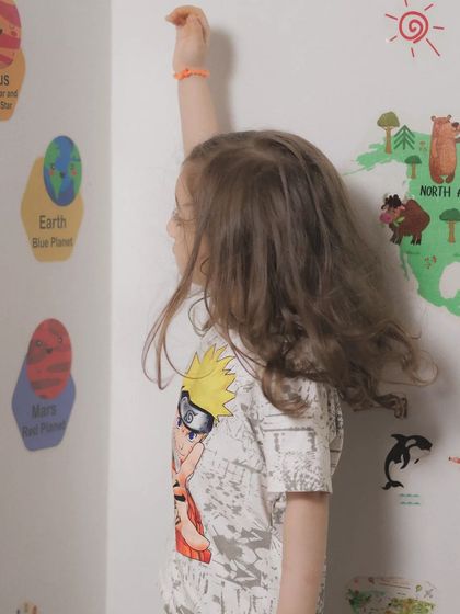 A child curiously measuring their height against a fun, educational wall chart. Capturing these small, everyday milestones is a wonderful way to document their growth.
