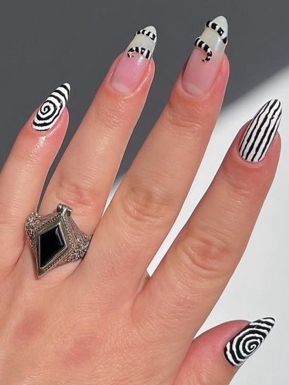 A bold, graphic black and white set with hypnotic swirls, stripes, and a tiny snake detail on stiletto nails.