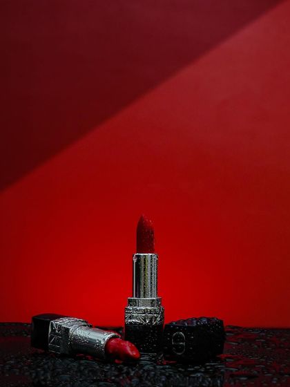 Painting the world, one shade at a time. A dramatic shot of Dior lipsticks on a wet, dark surface against a bold red background, creating a powerful and luxurious image.