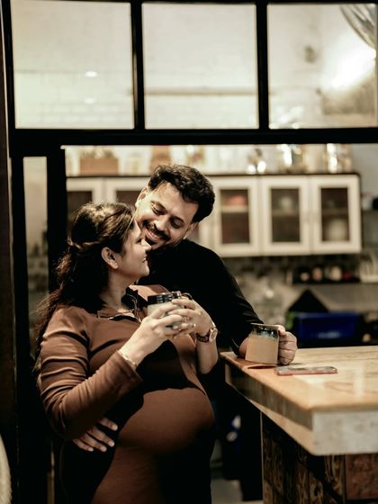 A happy, candid indoor shot of the couple sharing a coffee and a laugh. It shows the beauty in their everyday moments together.