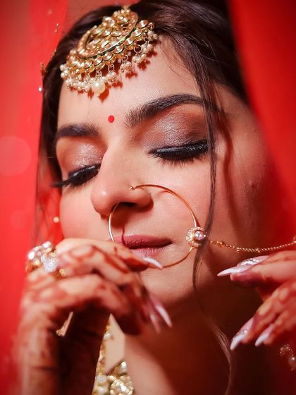 An intimate close-up of a bride, her face framed by her red veil, as she adjusts her nose ring.