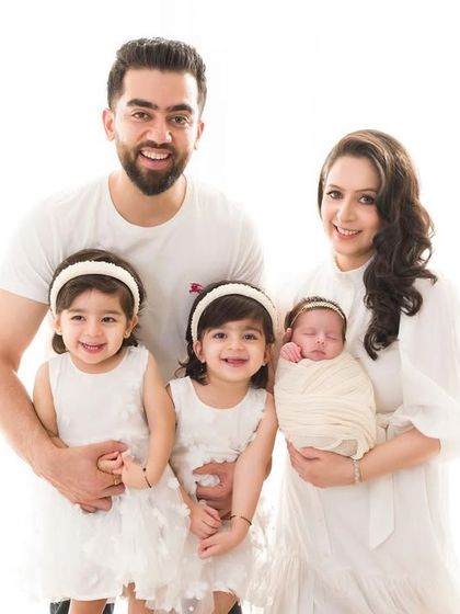 A perfect family portrait. The parents and their three beautiful daughters smile for a classic, timeless photograph in coordinated white outfits.