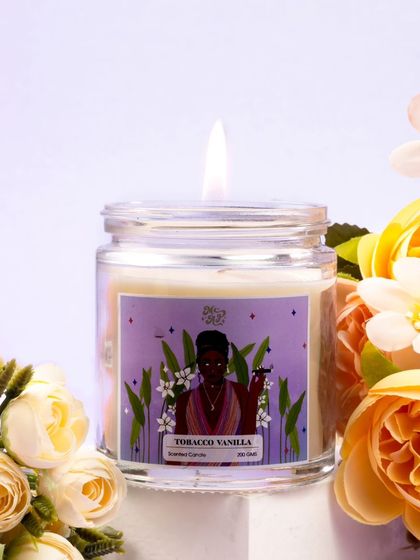 The rich purple label of the "Tobacco Vanilla" candle is beautifully framed by soft yellow and white flowers. This floral embrace adds a layer of softness and elegance to the warm, sophisticated scent.