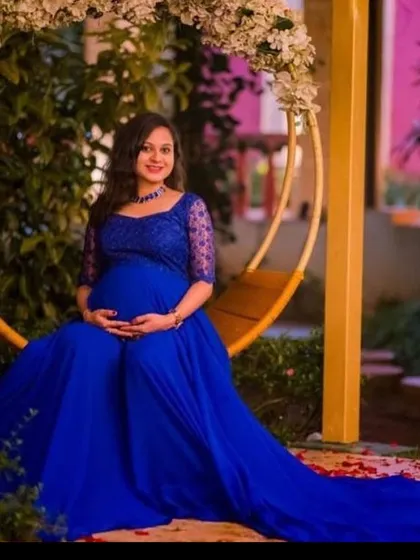 A peaceful maternity portrait. The mom-to-be is seated on a floral swing, wearing a royal blue gown that drapes beautifully around her.