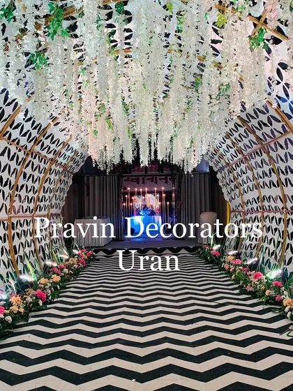We love creating unique passageways. This modern entrance tunnel features a custom-designed arched structure with geometric patterns, a ceiling of hanging white wisteria, and a stylish black-and-white carpet for a truly memorable walk-in.