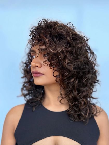 A profile shot that highlights the texture and dimension of these dark brown curls against a bright blue background.