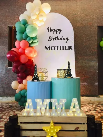 A special birthday decoration for a mother, with 'AMMA' in marquee letters and a simple, elegant balloon backdrop.