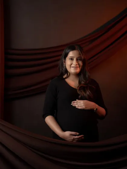A classic portrait against a dark, draped backdrop. The simple setup and direct gaze create a powerful and confident image of the mother-to-be.