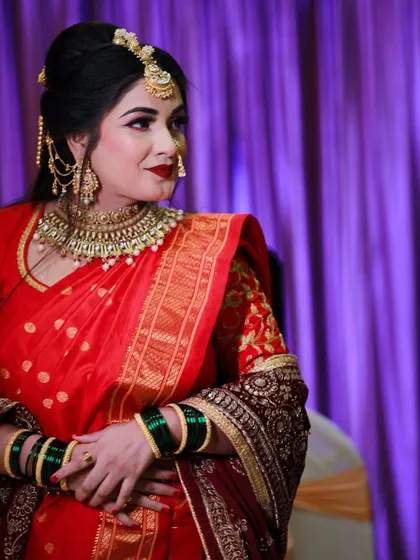 A candid shot of the bride during her engagement ceremony, looking elegant in a red saree against a purple backdrop.