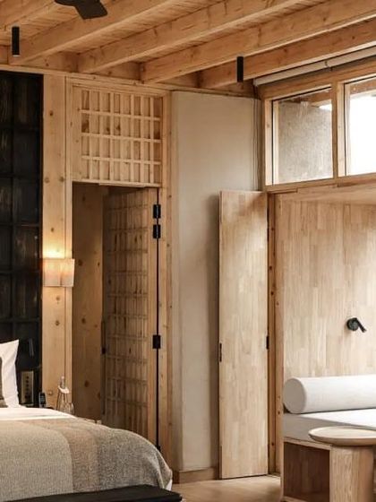 A bedroom in the Postcard hotel, showcasing a warm, minimalist aesthetic with natural wood and textiles. The design creates a cozy refuge that remains connected to the dramatic exterior environment.
