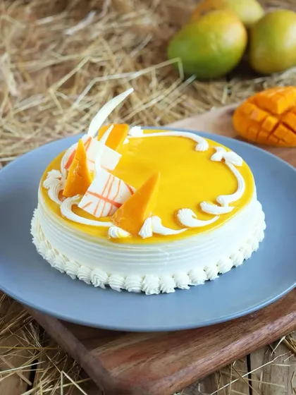 A simple yet elegant mango cake with a smooth mango glaze, decorated with white chocolate shards and fresh mango pieces.