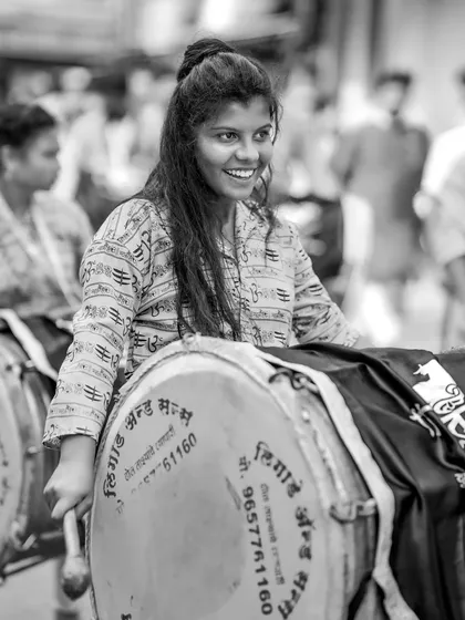 A black and white candid shot of a smiling female dhol player.