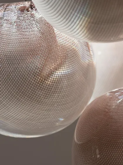 A macro detail of the Bocci 84 series. A bubble of white glass is blown through a copper mesh basket, which is then stretched, folded, and plunged into hot clear glass, creating this intricate texture.