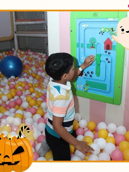 A little boy navigates the wall puzzle from inside the ball pit, combining physical and mental play.