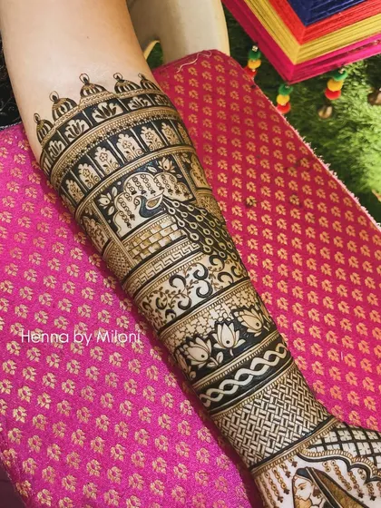 A close-up of the upper arm portion of a bridal mehendi. This section features intricate bands of peacocks, elephants, and lotus flowers.