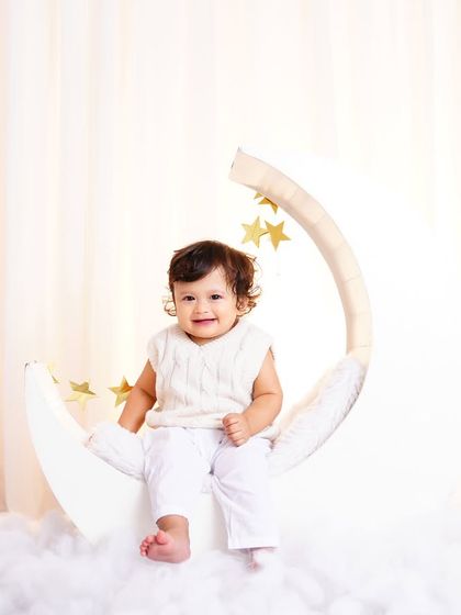 A happy baby boy sitting on a moon prop, surrounded by fluffy clouds. This is one of my favorite themes for milestone shoots.