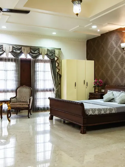 A spacious bedroom in the palace, featuring classic wooden furniture, a rich damask wallpapered accent wall, and elegant drapery, creating a cozy yet royal retreat.