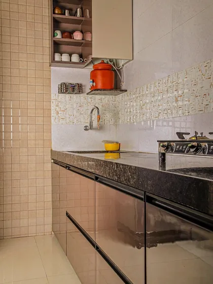 A warm and inviting kitchen with beige tiled walls, a black granite countertop, and handleless glossy cabinets.