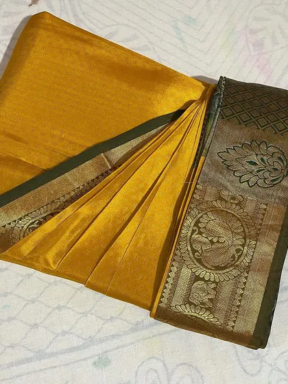 A mustard yellow saree with a traditional border, perfectly folded and ready for the wardrobe.