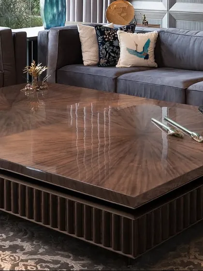 The centerpiece of this New Delhi farmhouse living room is a custom-designed coffee table with a starburst-patterned top in dyed figured veneer. Its substantial form is balanced by intricate wooden fluting and bronze detailing, creating a focal point that is both a statement and an invitation to gather.