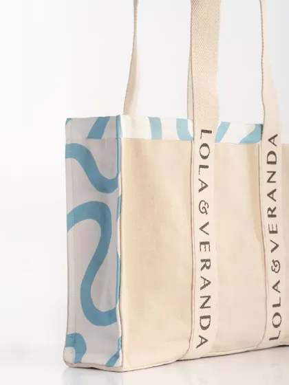 A close-up detail shot of a canvas tote bag, focusing on the printed logo and the side panel pattern. This clean, well-lit image is perfect for showing product quality and branding on an e-commerce site.