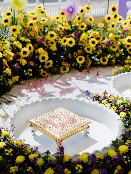 The traditional 'chowki' for the Haldi ritual, placed in a scalloped basin and surrounded by a dense ring of sunflowers and purple chrysanthemums.