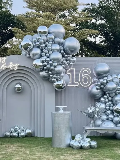 A modern and chic Sweet 16 party with a silver disco theme. The design uses a custom arched backdrop, neon "Happy Birthday" sign, and cascades of metallic silver balloons to create a sophisticated and photo-ready party space.