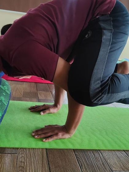 A student practices Kakkasana (Crow Pose) with a bolster for support. Using props is a smart way to understand the mechanics of an arm balance and build confidence before lifting off completely.