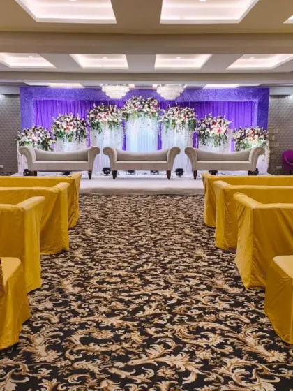 A grand stage with purple and white floral arrangements at Palm Beach banquet. The multi-level stage and plush seating add a sense of grandeur to the event.