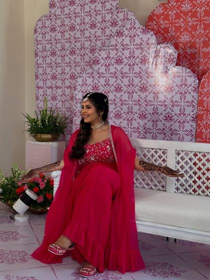 A wide shot of the bride, looking radiant in her pink outfit with her arms open to show the henna.