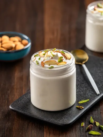 A creamy white jar dessert topped with chopped pistachios and almonds, styled simply to emphasize its texture and ingredients.