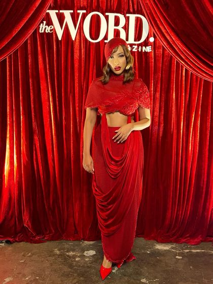 The full silhouette of the crimson cowl-drape set against a matching red backdrop, a look that is unapologetically bold.