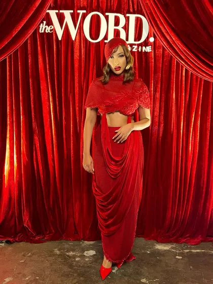 The full silhouette of the crimson cowl-drape set against a matching red backdrop, a look that is unapologetically bold.