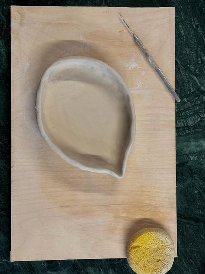 A freshly hand-built piece, a leaf-shaped dish, resting on a board with its tools. This is the beginning of its journey.