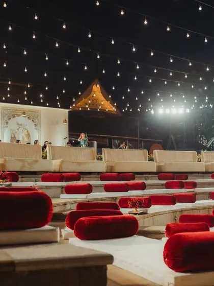 The amphitheater seating arranged for the wedding ceremony, with plush red velvet cushions on the stone steps. This setup provides guests with a clear, comfortable view of the grand mandap under the open night sky.